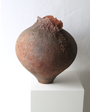 Rust colored ceramic vessel with dark opening and textured organic surface