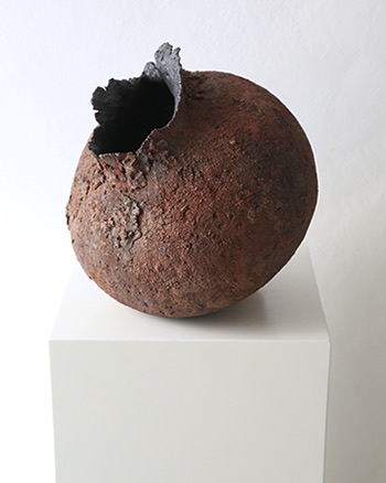 Dark rust ceramic vessel with rough stone-like surface and black opening