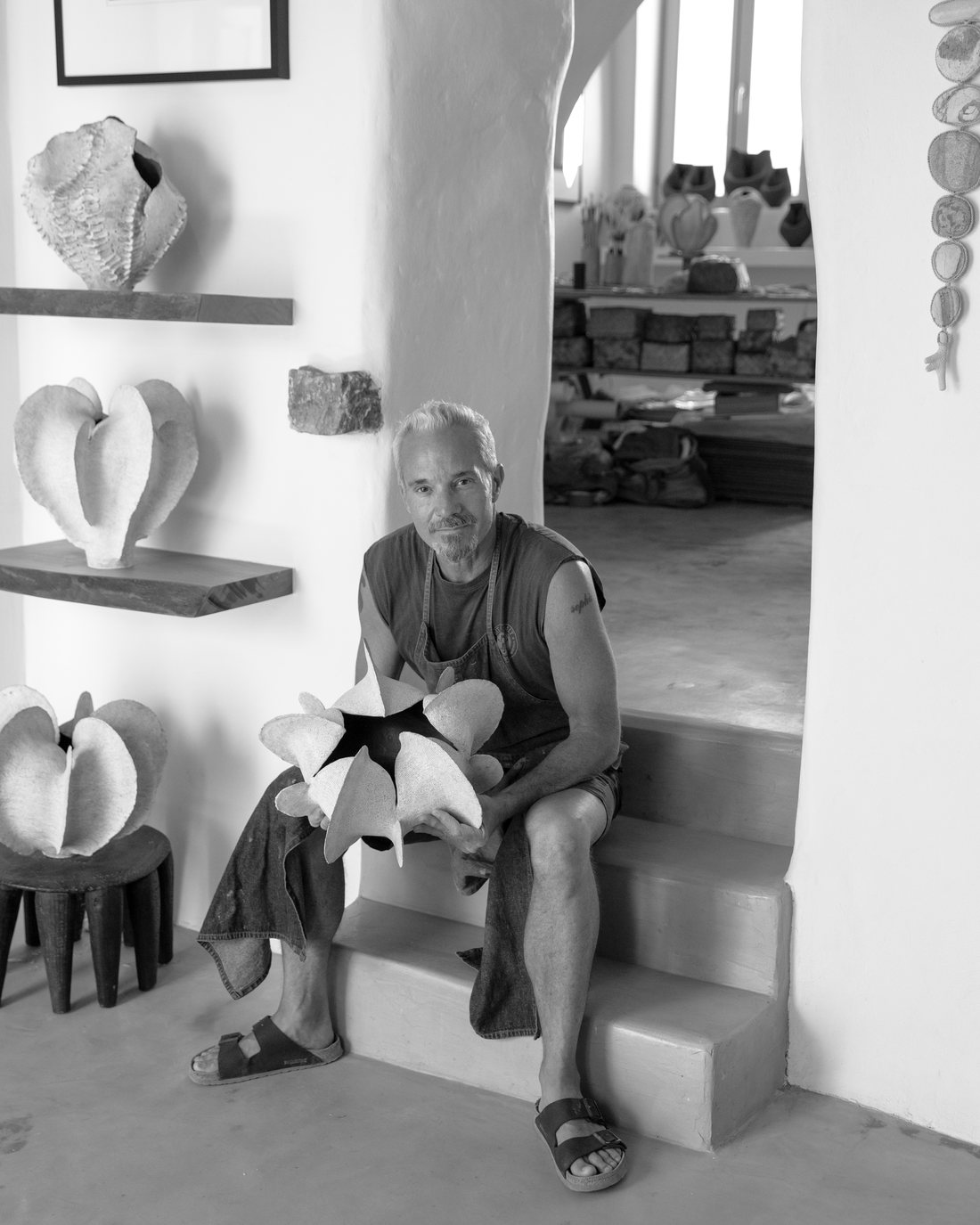 Todd Marshard seated in his Lefkes studio among shelves of ceramic forms