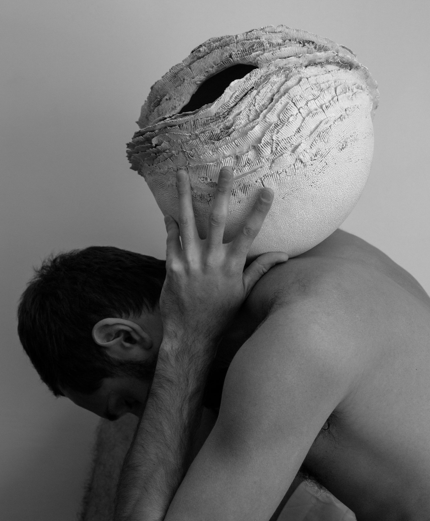 Model carrying a white textured ceramic vessel close to the shoulder