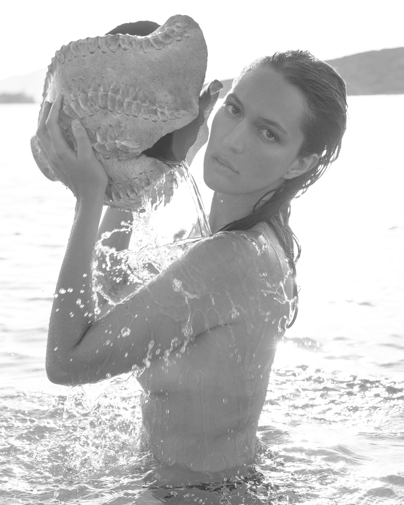 Model in the sea holding a textured ceramic vessel with water spilling through it
