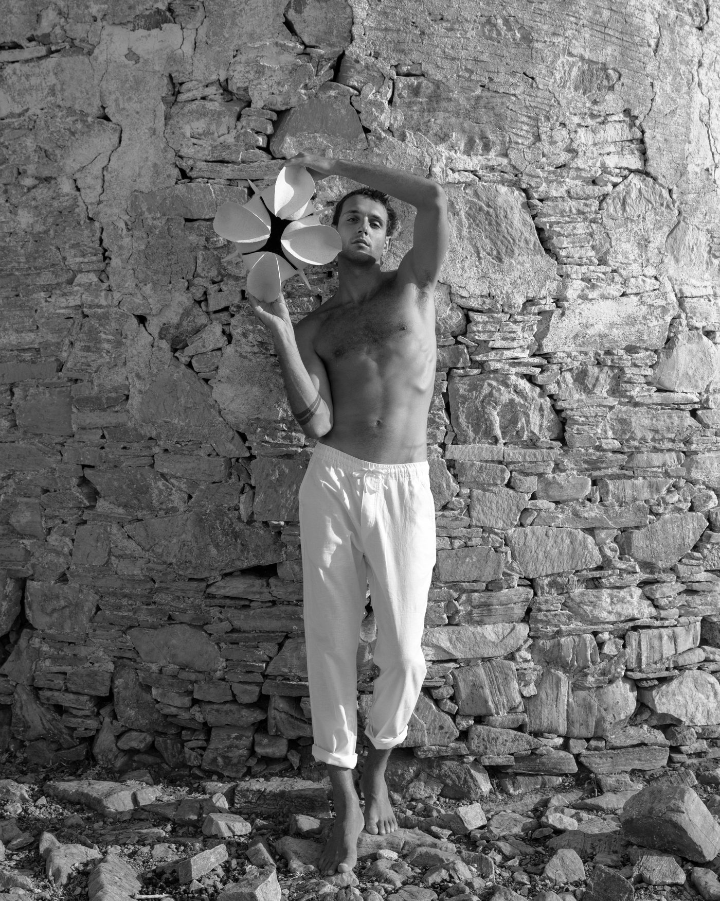 Model holding a white sculptural ceramic vessel against a Paros stone wall