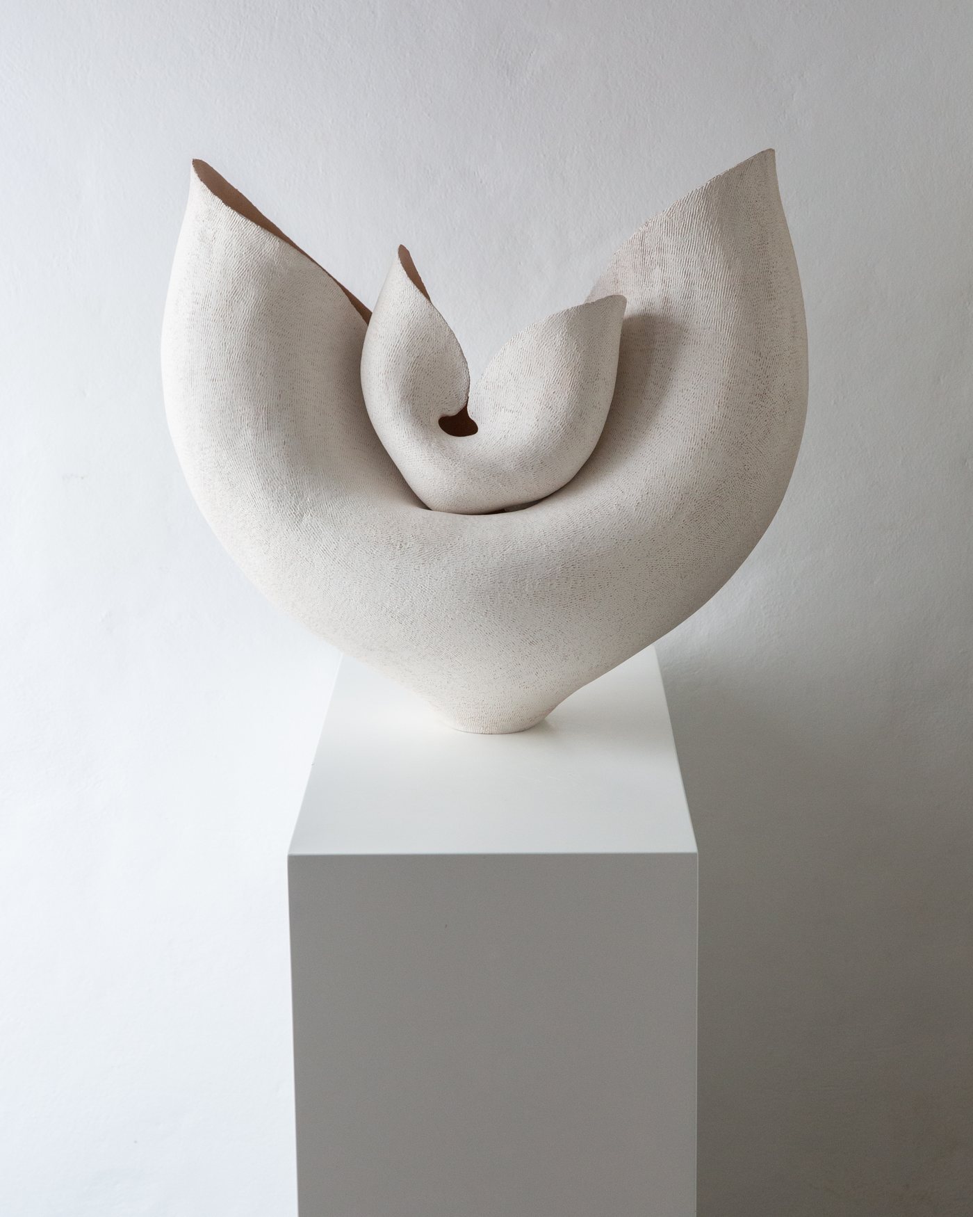 White sculptural ceramic form with lyre-like wings and terracotta edge